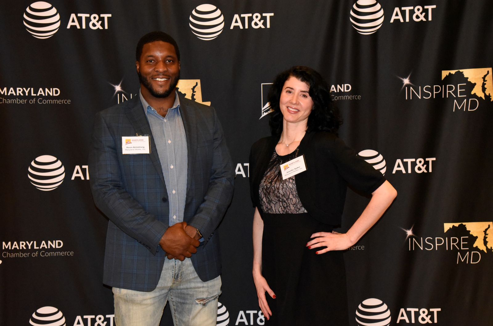 Two people smiling and posing in front of a step-and-repeat event backdrop featuring AT&T, Inspire MD, and Maryland Chamber of Commerce logos. Both are wearing business attire with name badges.