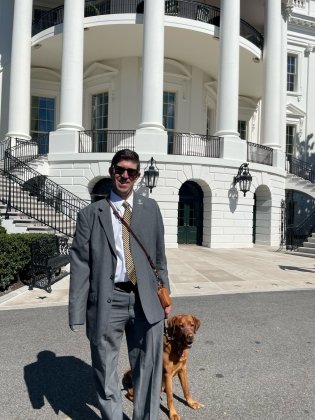 Image of Ryan Kules standing outside a government building with his dog.