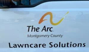 Logo and text on the side of a white vehicle that reads: ‘The Arc Montgomery County Lawncare Solutions’ with a stylized orange and yellow arc symbol above the text.