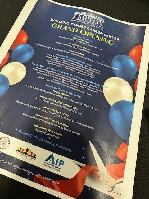 Flyer for the Grand Opening of the Employ Prince George’s Building Trades Career Center. The event features welcome remarks from Employ Prince George’s leadership, labor union representatives, and local officials. It highlights federal and state funding partners, including the U.S. Department of Labor and Maryland Department of Labor, as well as Prince George’s County Economic and Workforce System partners. The flyer lists featured speaker remarks from labor leaders, county executives, state delegates, members of Congress, and Governor Wes Moore. It announces a ribbon cutting and closing ceremony to celebrate the new center. The flyer is decorated with red, white, and blue balloons and an image of scissors cutting a ribbon, emphasizing the celebratory theme. Logos at the bottom include Employ Prince George’s, Apprenticeship Innovation Program, and partners.