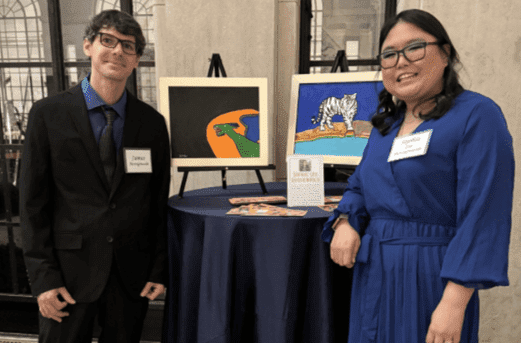 Chimes Virtual Gallery Featured Artist: Sophie Lee Rossignuolo; two people smiling to the camera stnading next to art work and a high top table.
