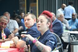 woman holding a microphone and speaking to a crowd sitting at a table